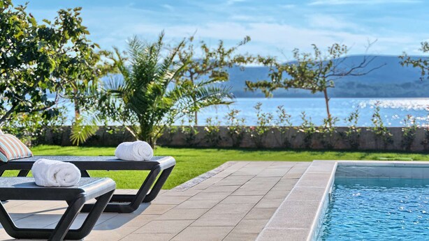 Zona de piscina con sillones de descanso y vista al mar.