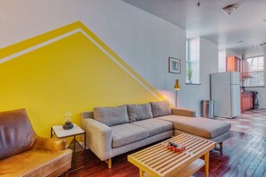 Relax in this stylish living space with a comfortable sofa, coffee table, and lamp, surrounded by a large window and kitchen area.