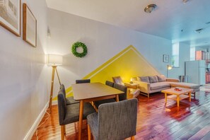 Relax in this stylish living room with a sofa, dining table, and coffee table, surrounded by a large window and a small plant.