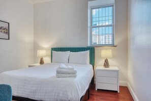 Cozy retreat with a neatly made bed, bedside table, and window with a grid pattern.