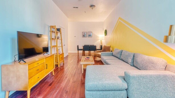 A modern living room with a TV, wooden furniture, a sofa, and a staircase with yellow accents. - Stairway | 3BR Apt w W/D Ideal for Groups (Philadelphia)