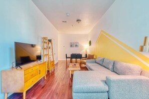 A modern living room with a TV, wooden furniture, a sofa, and a staircase with yellow accents. - Stairway | 3BR Apt w W/D Ideal for Groups (Philadelphia)