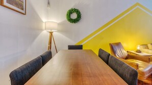 A conference room with a wooden table, four chairs, a floor lamp, a green wreath on the wall, and a yellow accent wall. - Stairway | 3BR Apt w W/D Ideal for Groups (Philadelphia)