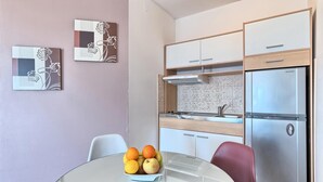 Eine kleine Küche mit Kühlschrank, Herd und Spüle, einem Esstisch mit Früchten und zwei Stühlen.
