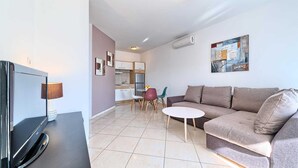 Ein modernes Wohnzimmer mit Flachbildfernseher, einer Couch, einem Couchtisch und einem Essbereich mit Stühlen und einem kleinen Tisch.