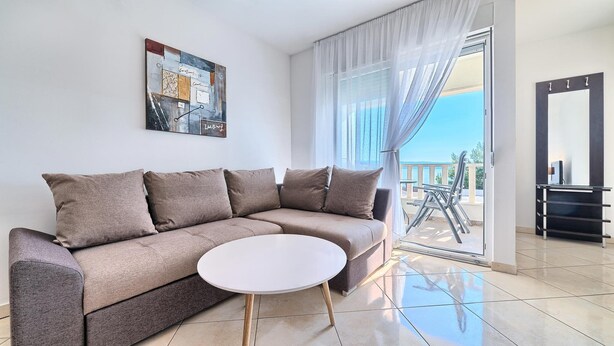 Ein modernes Wohnzimmer mit einem beigefarbenen Ecksofa, einem weißen Couchtisch und einem großen Fenster mit transparenten Vorhängen.