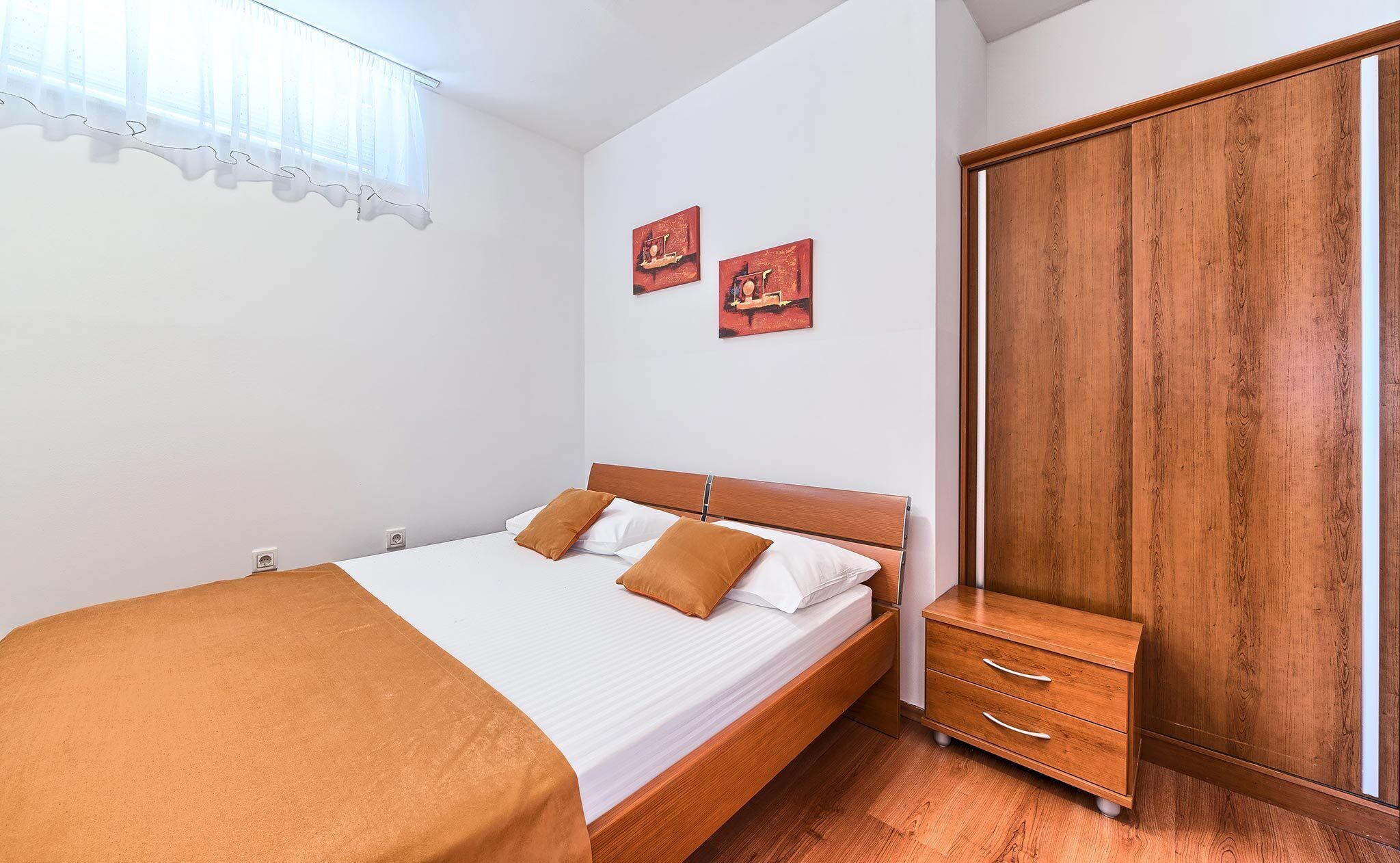 Un dormitorio con una cama de madera, un armario y dos cuadros en la pared.