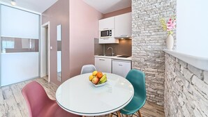 Una cocina compacta con microondas, pileta y lavavajillas Koncar. Un comedor con una mesa redonda y un frutero. Se observa una silla color turquesa.