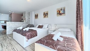 Habitación de hotel moderna con dos camas, una pared decorada con piedra, obras de arte en las paredes y vista al área de la cocina.