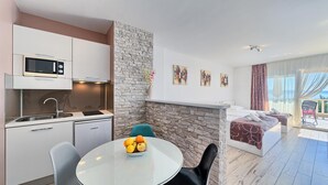 Una cocina moderna con microondas, lavamanos y un comedor con mesa y sillas. Se aprecia una pared de piedra, una cama con vistas y obras de arte en la pared.