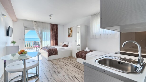 A modern hotel room with a balcony, a bed, a small table with chairs, and a kitchen area with a sink. - PANORAMIC APARTMENT WITH SEE VIEW (Podstrana)