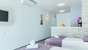 A modern hotel room with a large bed, a smaller bed, a vanity with a mirror, and a wall-mounted air conditioner.