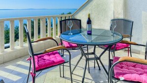 A balcony with a glass table, chairs, and a bottle of wine.