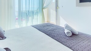 A hotel room with a bed, a TV mounted on the wall, and a view through a window with sheer curtains.