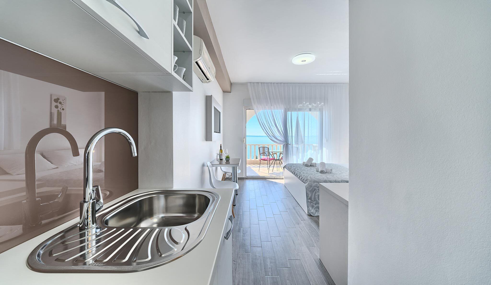 A modern kitchen with a stainless steel sink, a dining area with a table and chairs, and a balcony with a view of the sea.