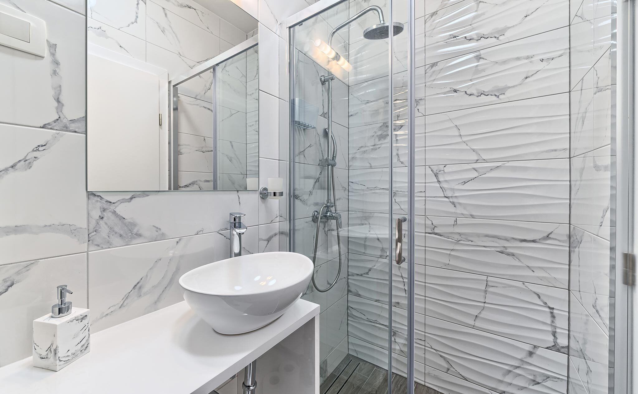 Un bagno moderno con un lavandino in marmo bianco, una cabina doccia in vetro e un grande specchio.