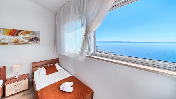 Habitació d'hotel amb un llit, una tauleta de nit, una làmpada, un quadre i una finestra amb vista al mar.