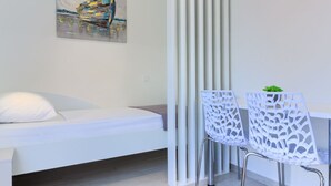 Una habitación moderna con una cama, dos sillas blancas, una mesa y un cuadro en la pared.