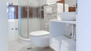 Un baño moderno con ducha envuelta en vidrio, inodoro blanco y tocador con lavamanos y toallero.