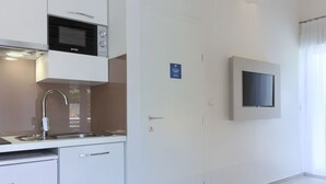 Una cocina moderna con microondas integrado, un lavamanos de acero inoxidable y lavavajillas. Hay un televisor de pantalla plana montado en la pared y una puerta con un cartel.