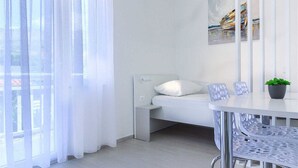 Un dormitorio moderno con cama, mesita de noche, una silla y una ventana con cortinas translúcidas.