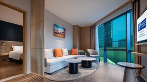 Habitación de hotel moderna con sofá, dos mesas redondas y un ventanal que ofrece vistas a la ciudad.