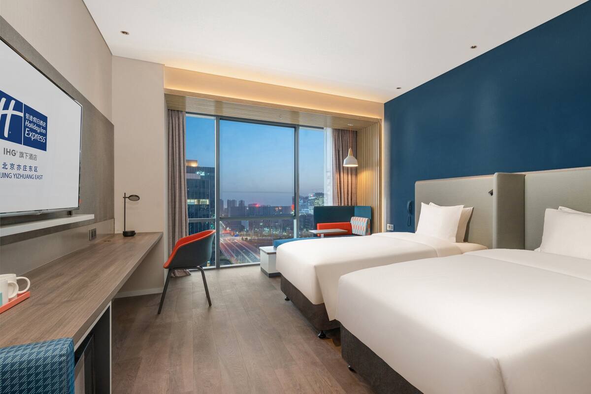 Une chambre d’hôtel avec deux lits, un bureau et une grande fenêtre donnant sur la ville.
