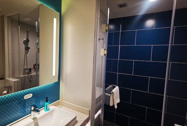 Une salle de bain avec un lavabo blanc, un miroir, une douchette à main et un porte-serviettes.