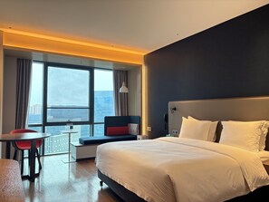 Ein Hotelzimmer mit einem großen Bett, einem Schreibtisch und Blick auf die Stadt.