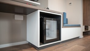 Eine kompakte Küche mit integriertem Kühlschrank, einer Mikrowelle und einer kleinen Sitzecke mit blauem Kissen.