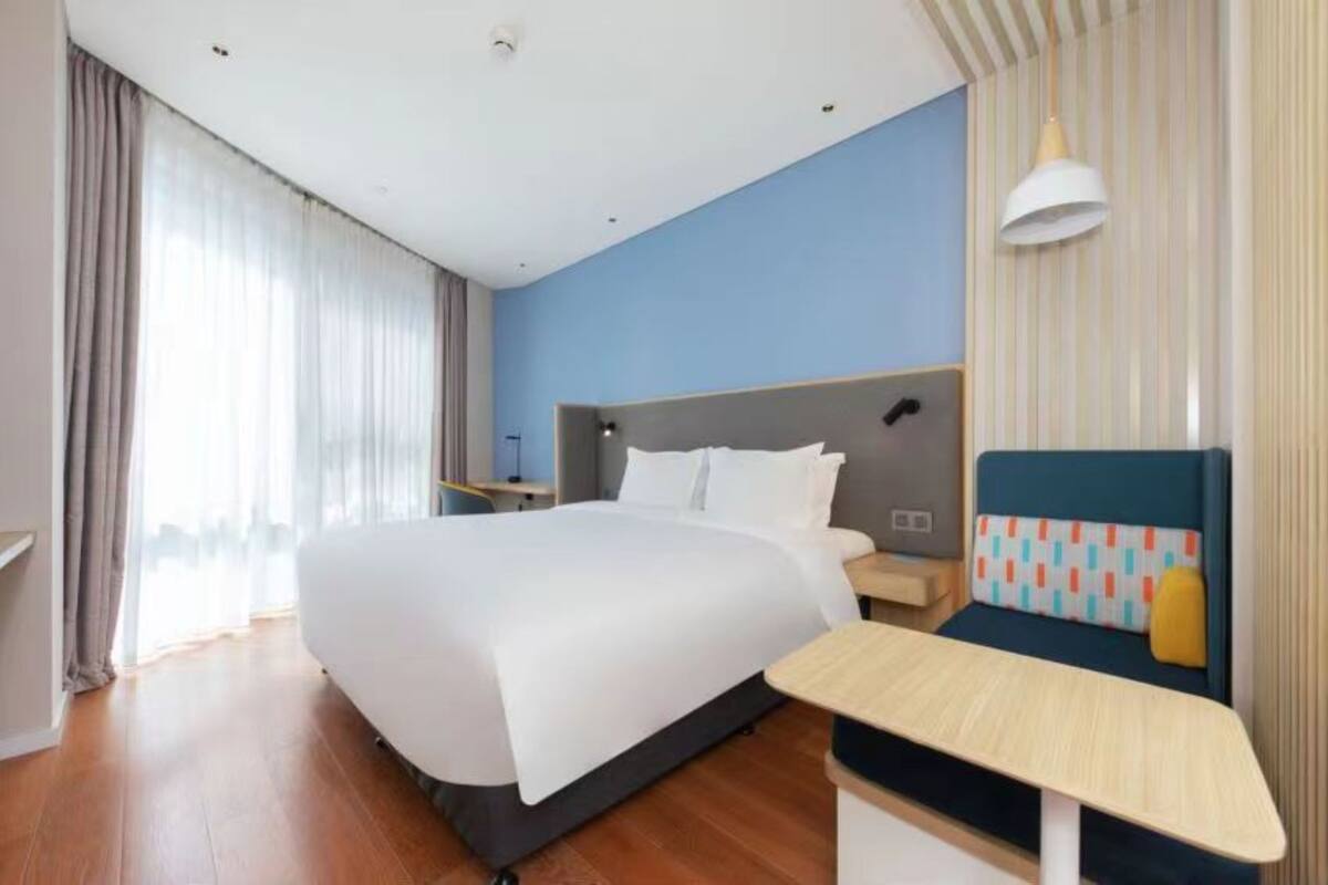 Une chambre d’hôtel avec un grand lit, une table de chevet, une chaise et une fenêtre avec des rideaux.