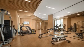 Une salle de sport moderne équipée de divers appareils d’exercice, dotée de planchers en bois et d’un grand miroir qui reflète l’espace.