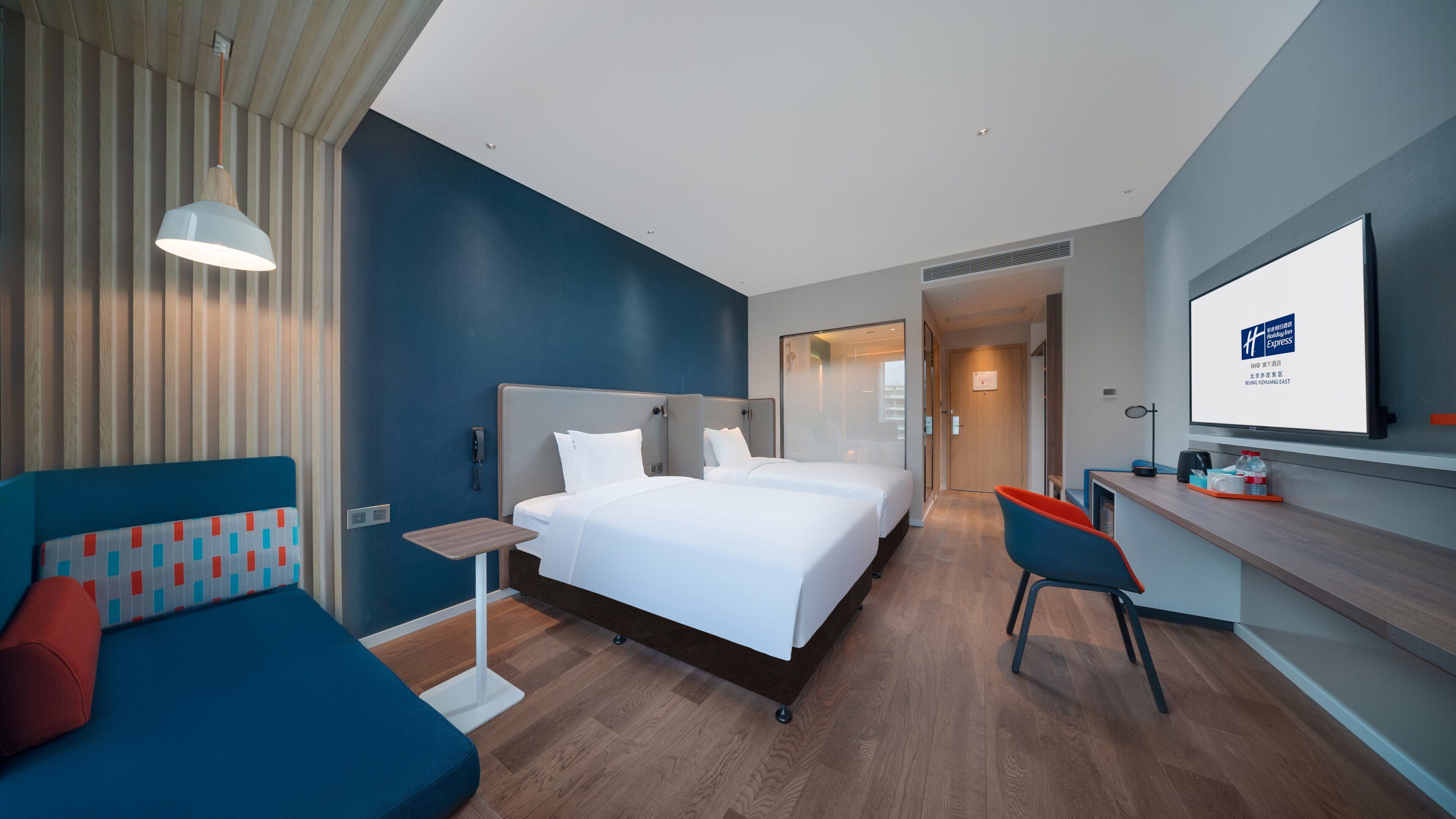 Ein modernes Hotelzimmer mit einem großen Bett, einem Schreibtisch, einem Sessel und einem Fernseher.