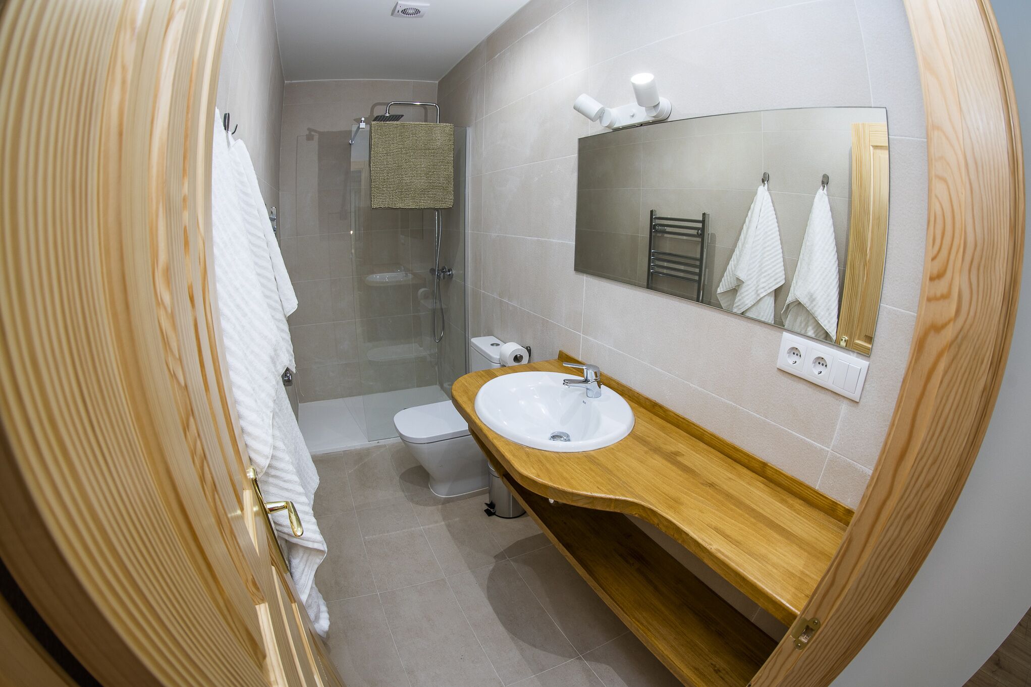 A modern bathroom with a wooden vanity, a large mirror, and a glass shower enclosure.
