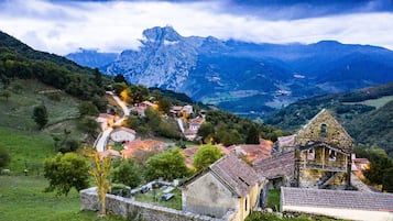 Un pueblo rural con edificios de piedra tradicionales, una iglesia y montañas al fondo.