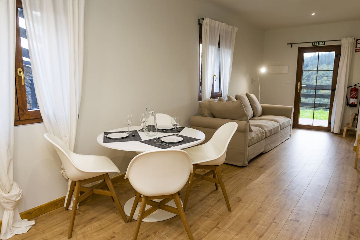 A dining area with a round table, two white chairs, and a beige sofa.