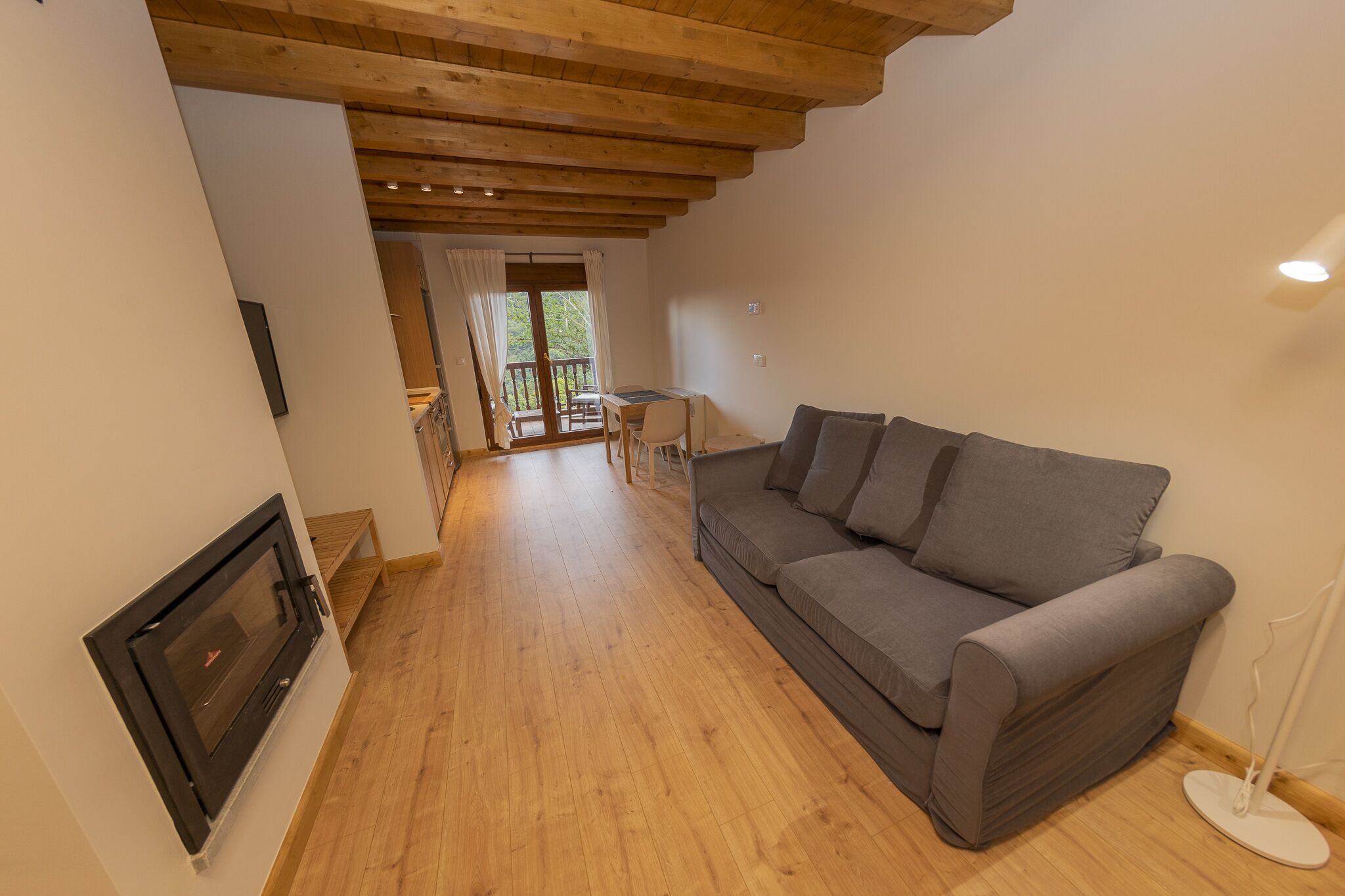 Una sala de estar con un sofá gris, piso de madera, una chimenea y un balcón con mesa y sillas.