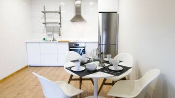 Una cocina moderna con armarios blancos, un refrigerador de acero inoxidable y un comedor con sillas blancas y mantel negro.