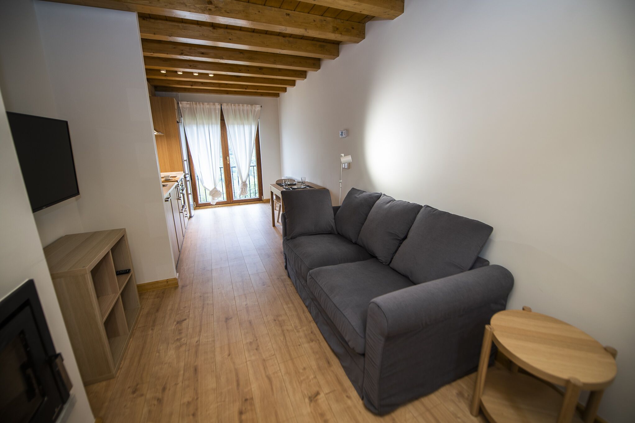 Ein Wohnzimmer mit grauem Sofa, einem Holztisch und einem an der Wand befestigten Fernseher.