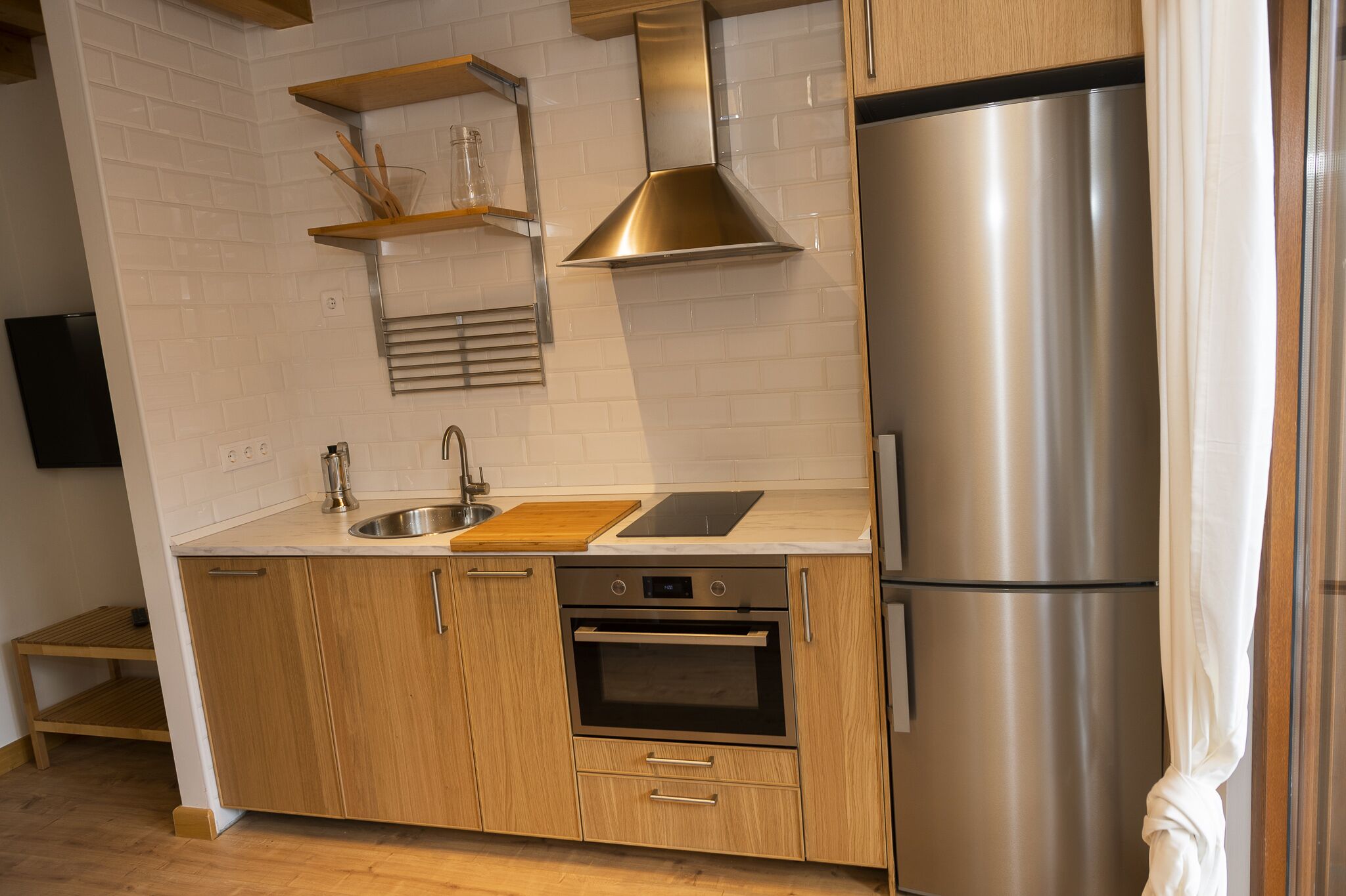 Una cocina moderna con electrodomésticos de acero inoxidable, armarios de madera y un salpicadero de azulejos blancos.
