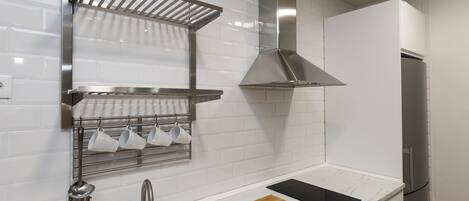 A modern kitchen with white subway tiles, stainless steel appliances, a wooden cutting board, and a metal rack for cups.