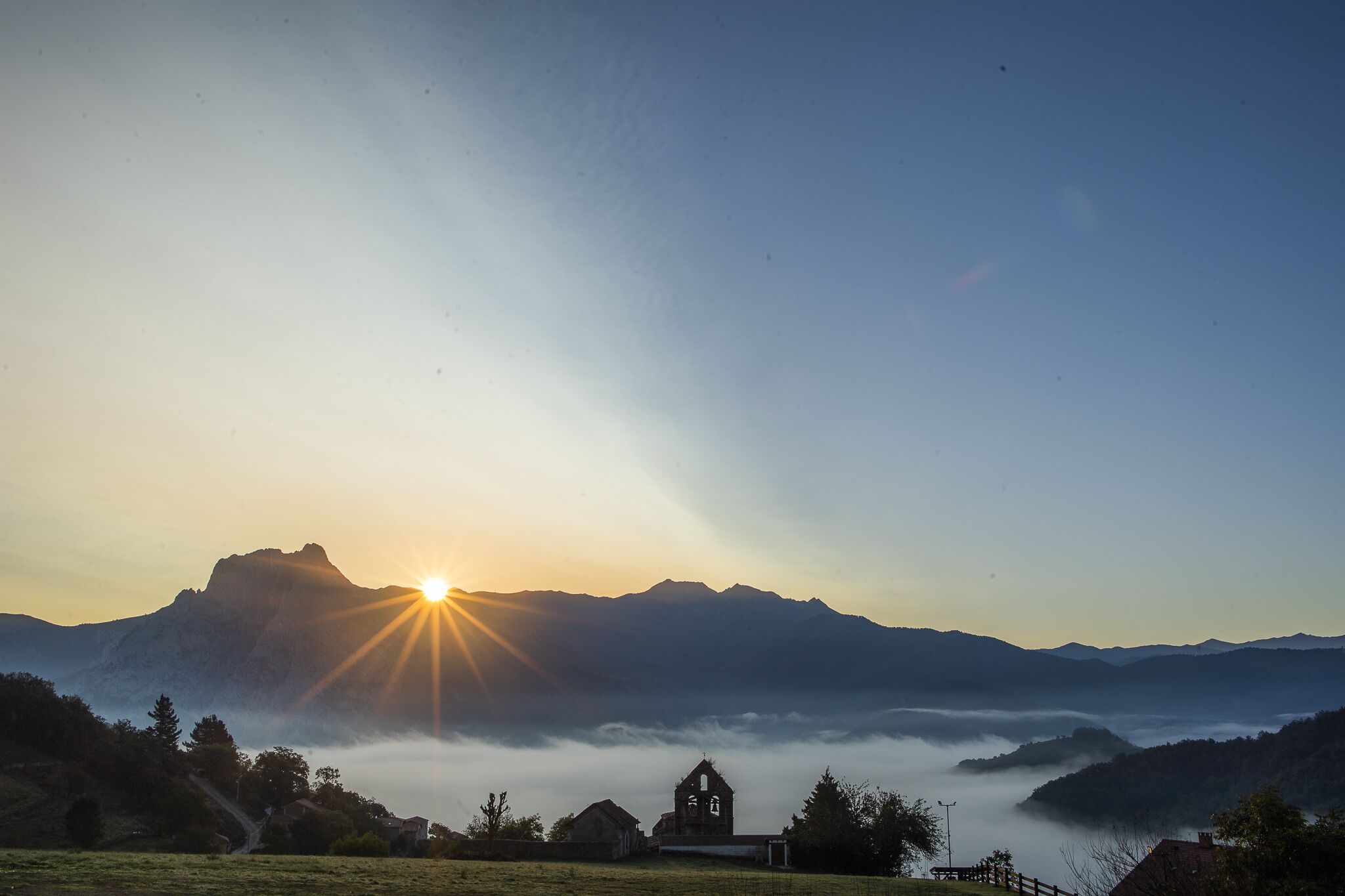 A mountain landscape with a church at sunset.