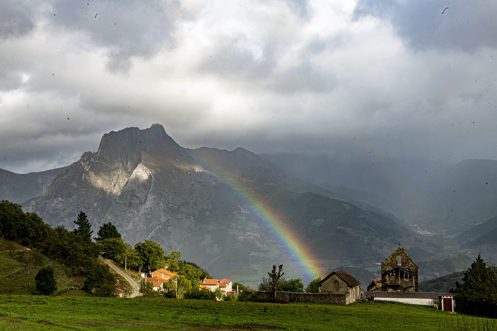 Un paysage de montagne avec un arc-en-ciel, des maisons et une église.