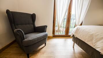 Een kamer met een grijze fauteuil, een bed met witte beddengoed en een houten vloer.