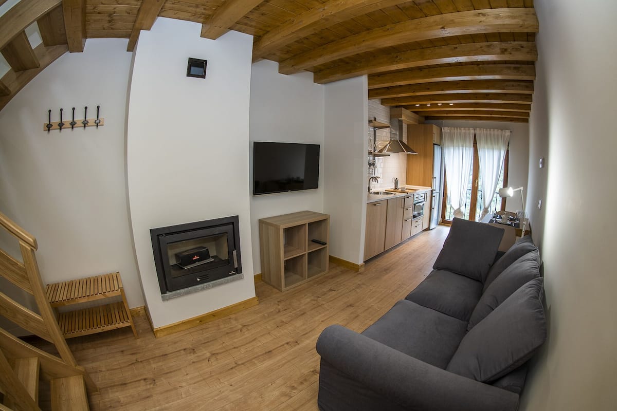 A modern living room with a fireplace, a flat-screen TV, a sofa, wooden flooring, and a staircase.