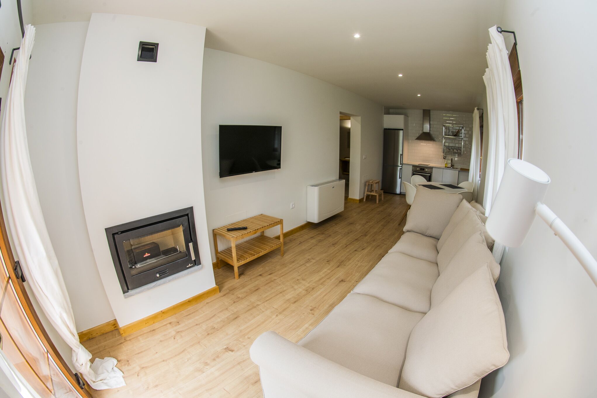 A modern living room with a sofa, a fireplace, a television, and a kitchen in the background.