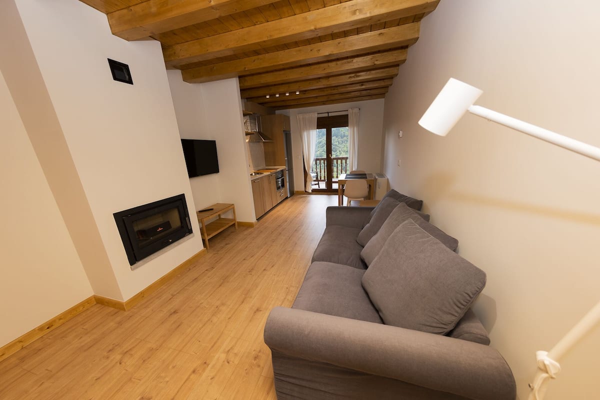 A modern living room with a wooden ceiling, a gray sofa, a fireplace, and a dining area with a table and chairs.