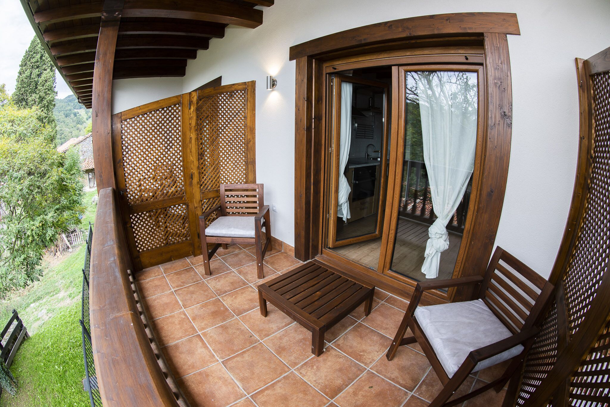 A balcony with wooden furniture, a sliding glass door, and a view of the surrounding greenery.