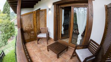 A balcony with wooden furniture, a sliding glass door, and a view of the surrounding greenery.