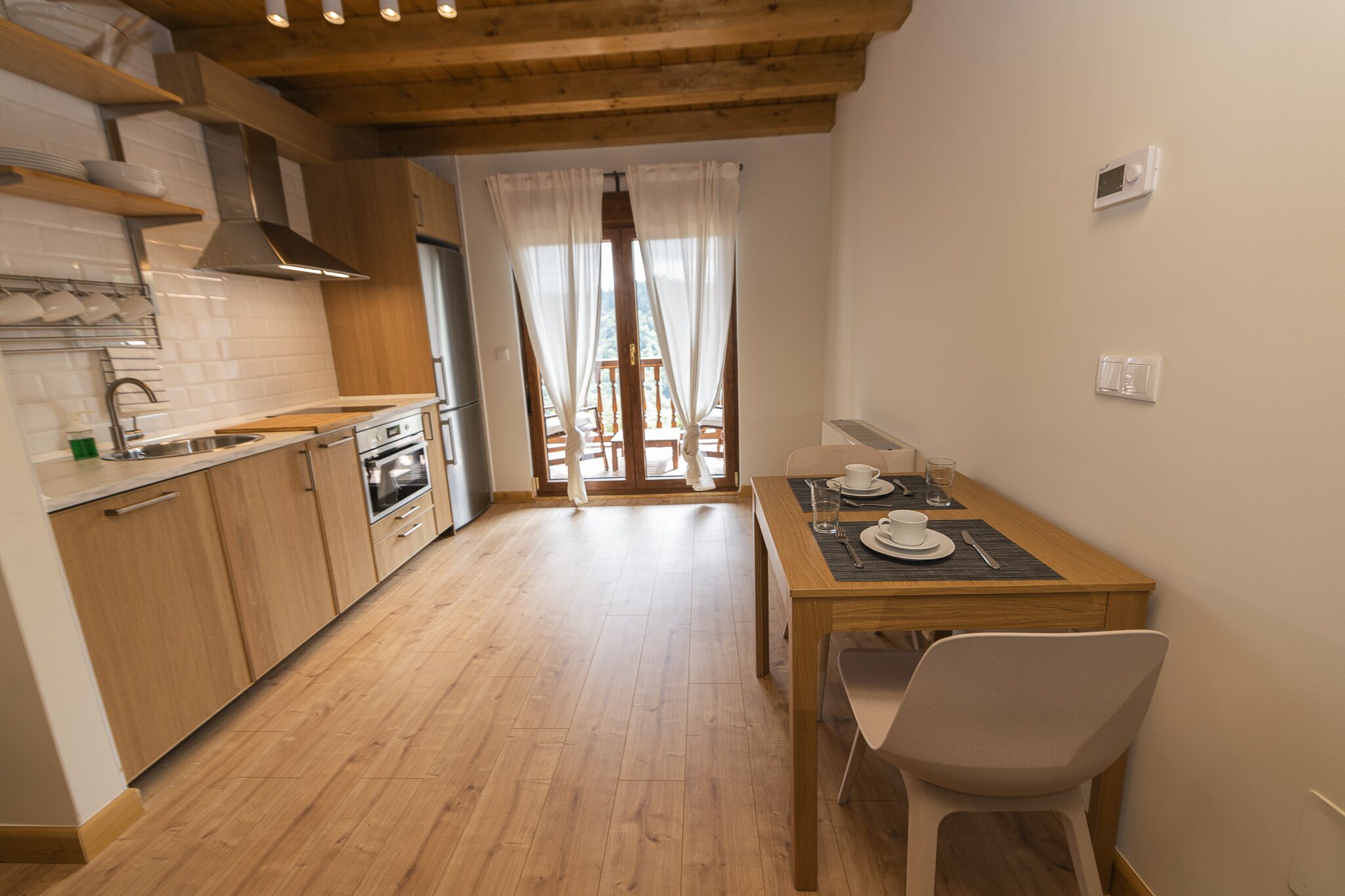 A modern kitchen with wooden cabinets, a built-in oven, and a dining area with a table and chairs.